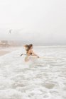Вид збоку молодої спортсменки з літаючим волоссям і дошкою для серфінгу в океані з піною під хмарним небом — стокове фото