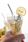 Crop unrecognizable person with glass of refreshing nonalcoholic pear cocktail with lemon slice and rosemary sprig — Stock Photo