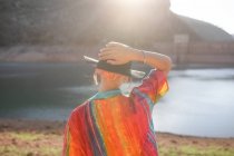 Back view woman looking at a lake with one hand holding a black hat — Stock Photo