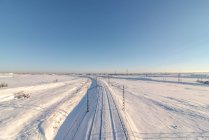 Drone vista del treno su ferrovia su terreno innevato sotto cielo blu chiaro — Foto stock