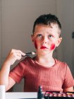 Charmantes Kind mit Make-up-Applikator berührt Kopf beim Wegschauen am Tisch mit Lidschattenpalette — Stockfoto