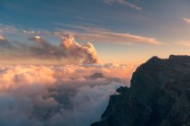 Sonnenaufgang auf mächtigen Berggipfeln inmitten weicher dicker weißer Wolken und im Hintergrund der Ausbruch eines Vulkans. Cumbre Vieja Vulkanausbruch auf La Palma Kanarische Inseln, Spanien, 2021 — Stockfoto