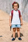 Schulkind mit Rucksack steht auf Gehweg und blickt im Sonnenlicht in Kamera — Stockfoto