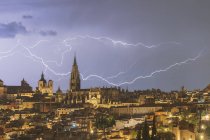 Cityscape of Toledo with high aged tower under cloudy sky with lightning during thunderstorm in night time — Stock Photo