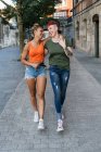 Vista posteriore di giovani donne omosessuali con tatuaggi che si abbracciano mentre camminano sulla passerella in città — Foto stock