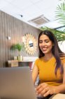 Lächelnde junge Unternehmerin sitzt am Tisch und blättert im Netbook, während sie an einem modernen Arbeitsplatz arbeitet — Stockfoto