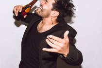 Веселий чоловік із закритими очима, що поливає пиво з пляшки на обличчі під час вечірки на білому тлі — стокове фото