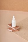 Kleine weiße Flasche Kosmetikserum auf gestapelten braunen Marmorsteinstücken auf Stoff auf beigem Hintergrund — Stockfoto