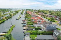 Drone vista de fachadas de edificios residenciales entre río y césped con árboles bajo el cielo nublado en la provincia de Utrecht Países Bajos - foto de stock