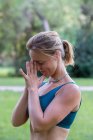Vista laterale della giovane donna in activewear in piedi con le mani namaste mentre pratica yoga nel parco verde durante il giorno — Foto stock