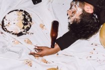 Зверху п'яний чоловік спить біля розбитого торта на день народження і порожня пляшка під час вечірки — стокове фото