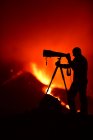 Vue latérale de la silhouette d'un homme enregistrant et photographiant avec un trépied l'explosion de lave sur les îles Canaries de La Palma 2021 — Photo de stock