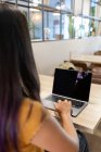 Vista posterior de una joven empresaria irreconocible sentada a la mesa y navegando por netbook mientras trabaja en un lugar de trabajo moderno - foto de stock