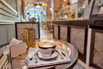 Керамическая чашка ароматного кофе с искусством латте на столе с салфетками и цветущей розой в столовой — стоковое фото