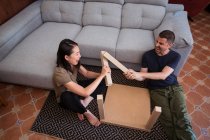 Multiracial couple assembling table on rug in house — Stock Photo