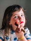 Criança com aplicador fazendo face com produtos cosméticos variados em casa olhando para a câmera — Fotografia de Stock