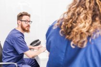 Ein bärtiger Sanitäter in Uniform und Brille tippt auf der Tastatur, während er mit einem Arzt im Krankenhaus arbeitet — Stockfoto