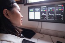 Сторона зору концентрованої азіатської жінки, що працює на комп'ютері з графіками, що показують динаміку змін в вартості криптовалют на зручному робочому місці. — стокове фото