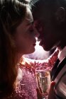 Вид сбоку на кукурузную пару со стаканом на шампанском в момент поцелуя с блестящим световым лучом, смотрящим друг на друга во время вечеринки — стоковое фото