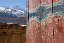 Antigua pared de madera con arañazos y pintura agrietada de edificio rodeada de altas cumbres nevadas en Nepal - foto de stock