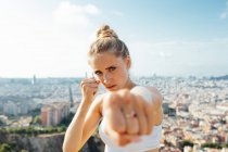 Жінка-боксер кричить, показуючи техніку удару і дивлячись на камеру під час тренування в сонячному місті — стокове фото