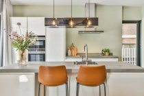 Rubinetto in acciaio inox con lavabo in bancone sotto lampade brillanti in cucina elegante in casa moderna — Foto stock
