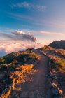 Lever de soleil sur un sentier de montagne de haute altitude au milieu de nuages blancs doux et épais et l'éruption d'un volcan en arrière-plan. Éruption volcanique Cumbre Vieja à La Palma Îles Canaries, Espagne, 2021 — Photo de stock