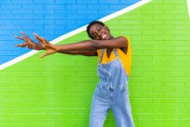 Feliz joven mujer afroamericana sonriendo mientras está de pie en la pared brillante colorido - foto de stock
