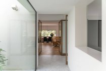 Corridoio stretto con pareti in vetro che conduce a ampio soggiorno con comoda poltrona e zona pranzo in villa contemporanea alla luce del giorno — Foto stock