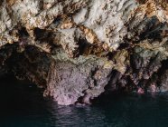 Agua de mar transparente y ondulada que fluye a través de una cueva rocosa áspera con salientes irregulares afilados - foto de stock