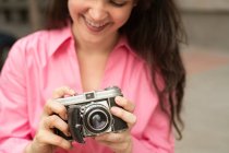 Cropped young happy female with long brown hair taking picture on old fashioned photo camera on street in city — Stock Photo