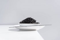 From above of ceramic bowl with delicious spaghetti with black squid ink with chopsticks on grey background — Stock Photo