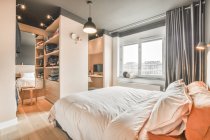 Comodo letto con biancheria leggera posizionato di fronte armadio e specchio in camera da letto elegante durante il giorno — Foto stock