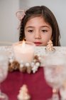 Enfant tendre contemplant une bougie flamboyante en verre sur une table avec des cônes de conifères pendant les vacances du Nouvel An à la maison — Photo de stock