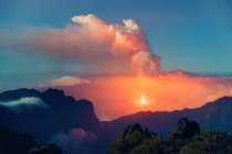 Nächtliche Landschaft mit einem ausbrechenden Vulkan im Hintergrund und einem Wolkenmeer, das die Berge von einem bewachsenen und felsigen Berg bedeckt. Cumbre Vieja Vulkanausbruch auf La Palma Kanarische Inseln, Spanien 2021 — Stockfoto