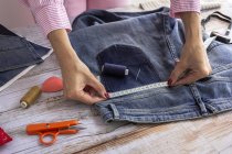 High angle of crop anonymous female dressmaker measuring jeans pocket on wooden table in daytime — Stock Photo