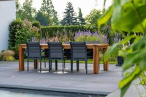 Mesa de comedor con silla y tumbonas de madera situadas cerca de la piscina en el patio de la costosa villa minimalista contemporánea en un día soleado - foto de stock