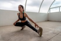 Giovane sportiva etnica flessibile in abbigliamento attivo stretching gamba durante l'allenamento durante il giorno — Foto stock