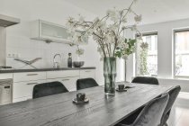 Interieur der modernen hellen Küche und Essbereich mit großem Tisch mit Blumenstrauß und Stühlen in einer modernen Wohnung tagsüber — Stockfoto
