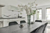 Interior da cozinha de luz contemporânea e zona de jantar com grande mesa com buquê de flores e cadeiras no apartamento moderno durante o dia — Fotografia de Stock