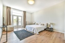 Moderna spaziosa camera da letto arredata con comodo letto con comodino vicino moquette e balcone — Foto stock