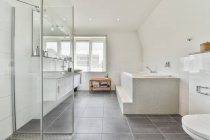 Interior do banheiro contemporâneo com chuveiro contra banheira e janela em casa com piso em azulejo — Fotografia de Stock