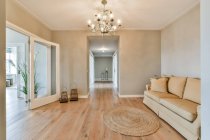 Geräumiges, modernes Wohnzimmer mit bequemem Sofa und Teppich unter Kronleuchter im Tageslicht — Stockfoto