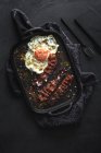 Vue du dessus de l'oeuf latéral ensoleillé avec tranches de bacon frit et condiments sur plateau contre des couverts sur fond sombre — Photo de stock