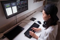 Высокоугольный боковой вид концентрированной азиатской женщины, работающей за компьютером, с графиками, показывающими динамику изменения стоимости криптовалюты на удобном рабочем месте — стоковое фото