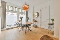 Moderno interno della sala da pranzo con tavolo in legno e sedie in plastica sotto lampadario creativo in spazioso nuovo appartamento — Foto stock
