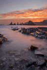 Paysage spectaculaire avec des vagues de mer mousseuses lavant des formations rocheuses rugueuses de différentes formes sur la plage sauvage de Geirua dans les Asturies en Espagne pendant le coucher du soleil — Photo de stock