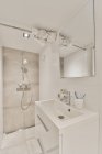 Modernes Badezimmer mit Keramikwaschbecken unter Spiegel gegen Duschbad mit Lampe im Haus — Stockfoto