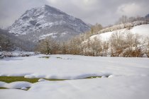 Пейзаж горных склонов и долины покрытые белым снегом с небольшим сельским домом под голубым облачным небом в природном парке Redes, расположенном в Калео-Астуриас, Испания — стоковое фото