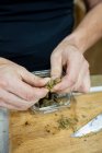 Alto angolo di coltura irriconoscibile maschio premendo pianta di marijuana essiccata pezzo sopra il contenitore sul tavolo — Foto stock